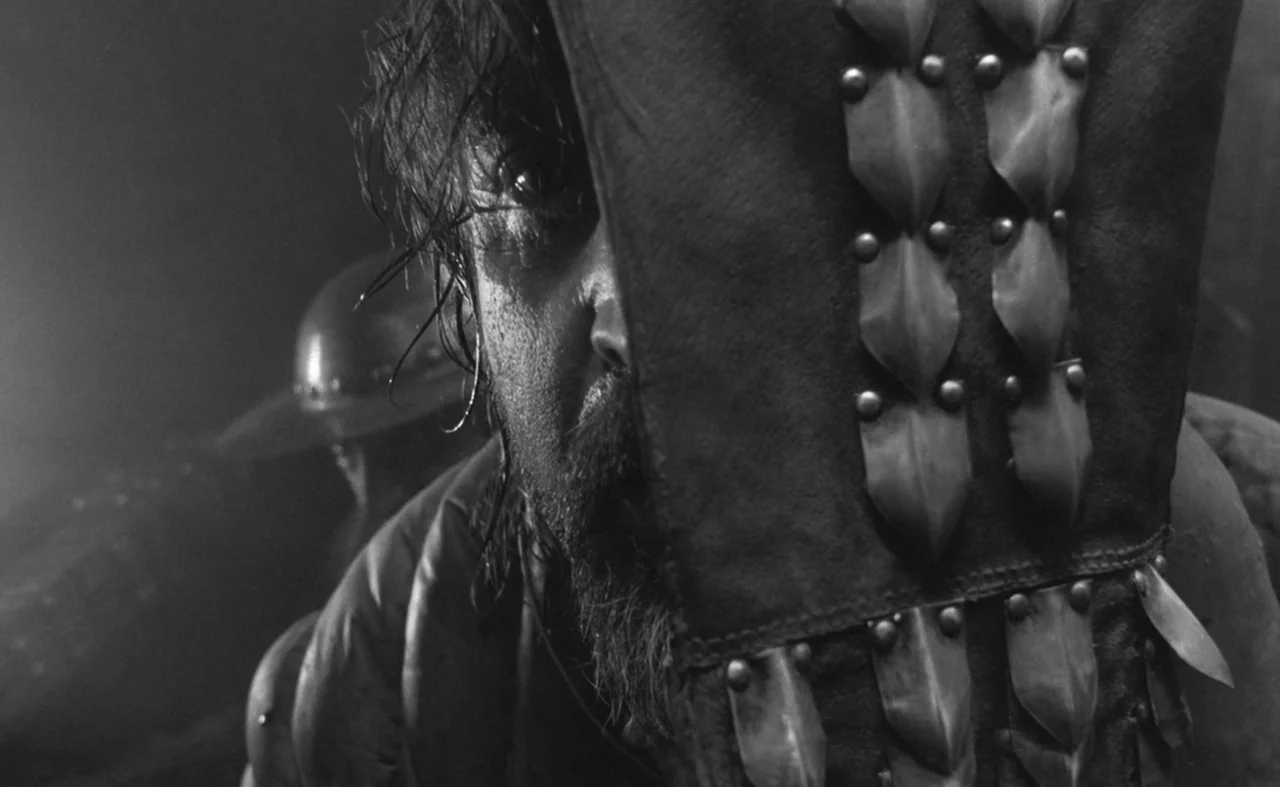 Hard To Be A God (2013) movie still: closeup — A dark, atmospheric medieval battlefield scene with smoke or dust obscuring the background. A man…