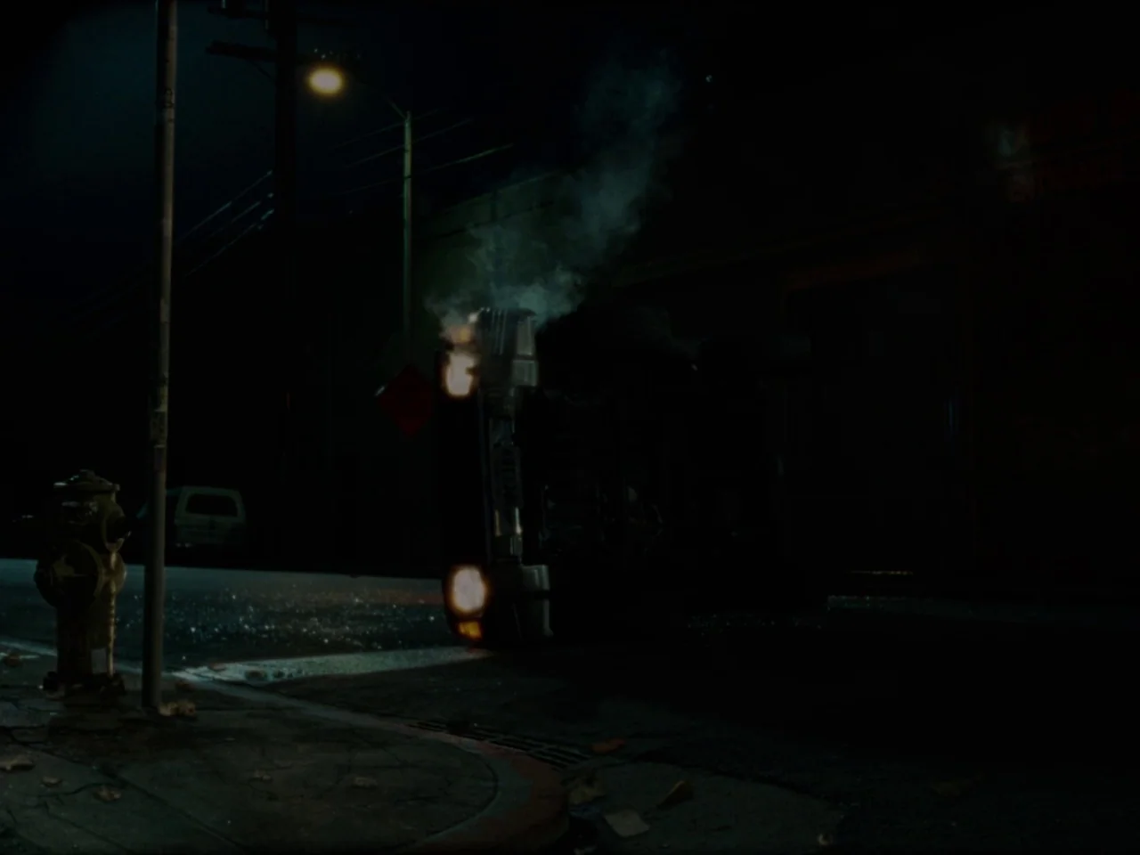 Mid90s (2018) movie still: wide — A dark, empty city street at night features a fire hydrant on the sidewalk. A car is overturned on the asphalt,…