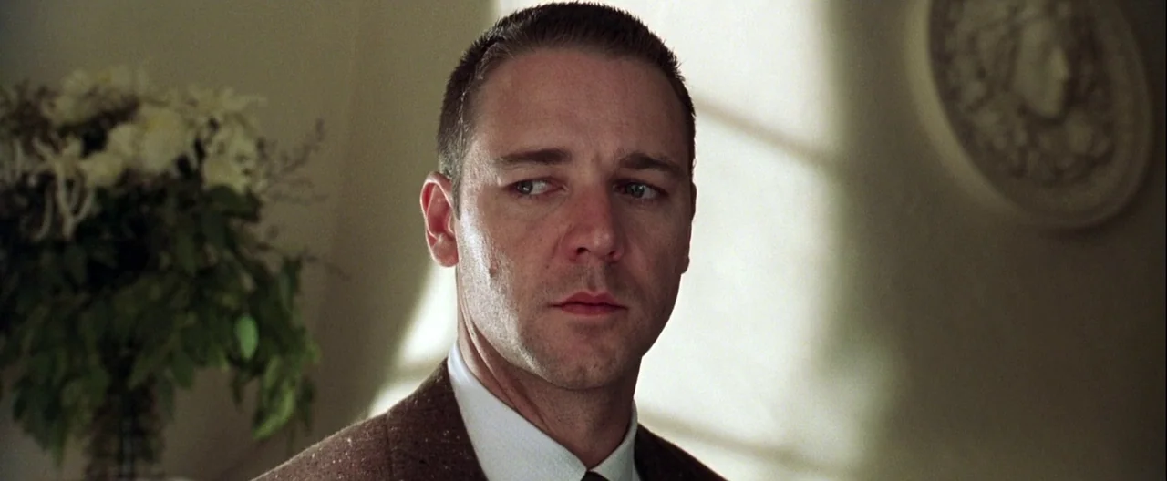 L.A. Confidential (1997) movie still: closeup — A well-lit interior room features a white wall with a decorative circular plaster relief. A man…