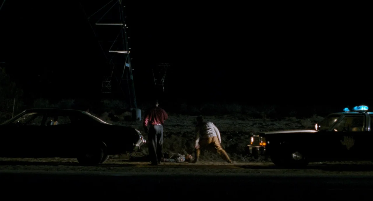One False Move (1991) movie still: wide — A dark, desolate stretch of desert road at night features two cars parked side-by-side. Three men are…