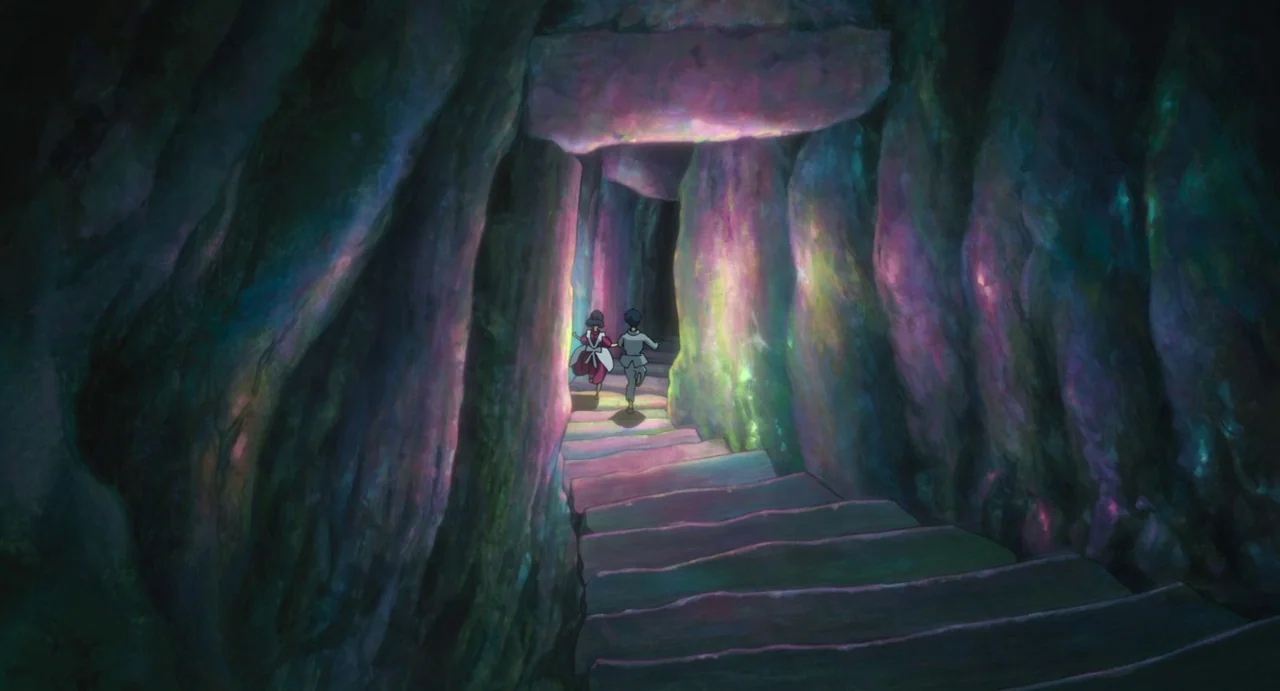 The Boy and The Heron (2023) movie still: wide — A dark subterranean passage is lined with uneven rock walls exhibiting multicolored glowing…