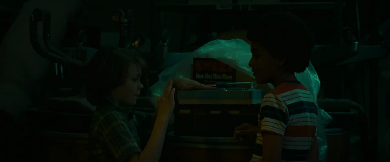 Wonderstruck (2017) movie still: medium — A dark, cluttered room contains stacked crates and a portable record player under plastic. Two boys stand…