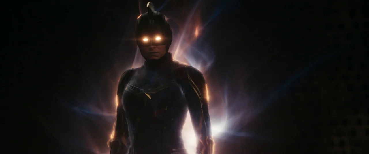 The Marvels (2023) movie still: medium — A figure stands in a dark, indistinct environment surrounded by swirling wisps of energy. The subject wears…