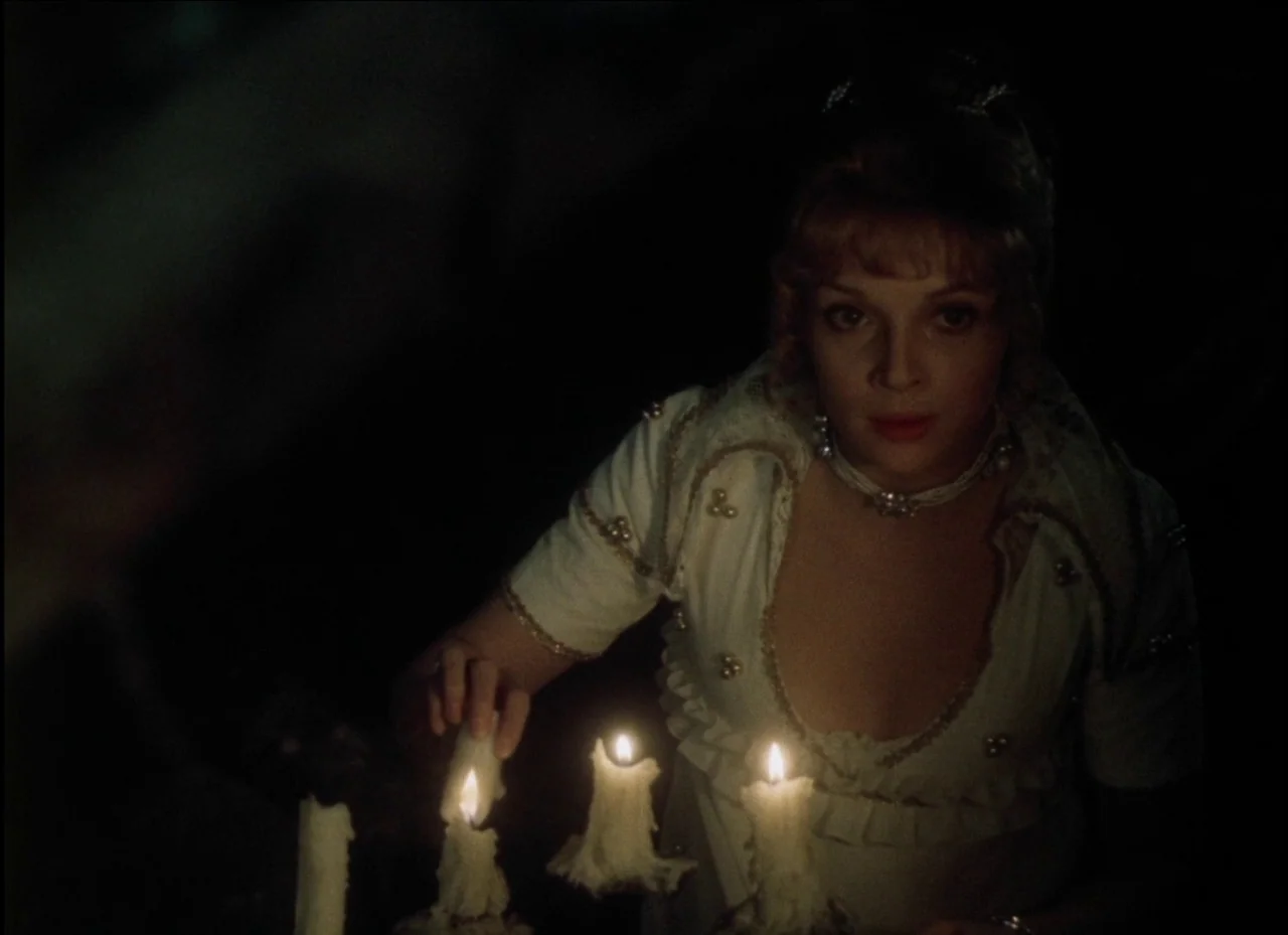 Beauty and the Beast (1979) movie still: medium — A dimly lit room features a woman in a period gown centered in darkness. She reaches forward to…