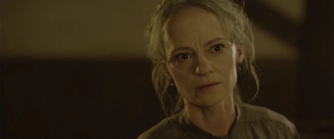 Ghosts of the Ozarks (2022) movie still: closeup — A dimly lit interior space with dark, indistinct walls surrounding the central subject. A…