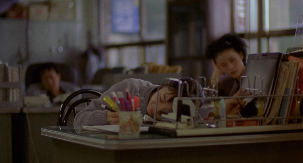 Barking Dogs Never Bite (2000) movie still: medium — An office environment with desks, paperwork, and office supplies scattered across the surfaces.…