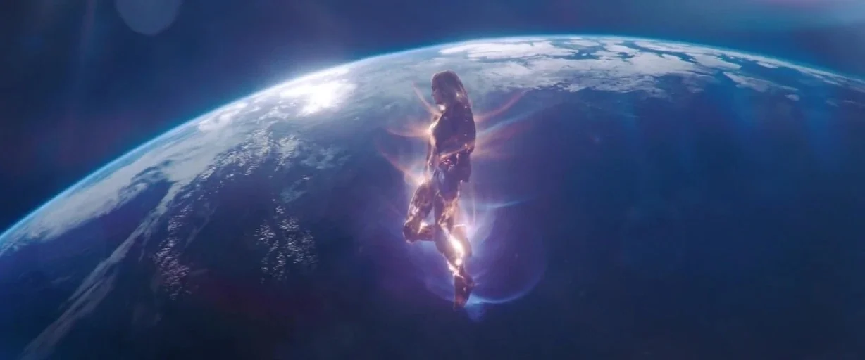 Captain Marvel (2019) movie still: wide — The curved horizon of the Earth is visible against the darkness of outer space. A glowing female figure…