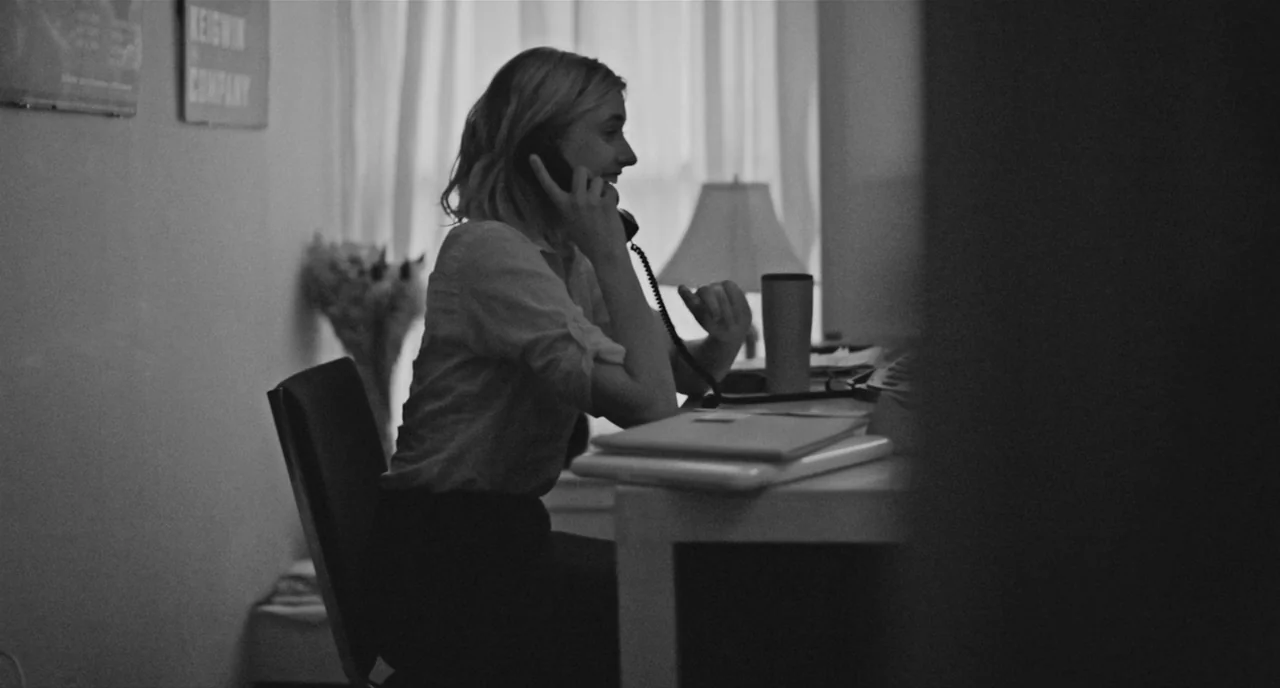 Frances Ha (2012) movie still: medium — A quiet work area contains a desk cluttered with notebooks and a beverage container. A woman wearing a light…
