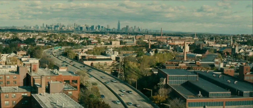 Be Kind Rewind (2008) movie still: establishing — A wide aerial view of a city highway flanked by industrial buildings and houses. The distant…