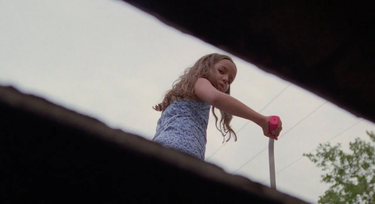 Boyhood (2014) movie still: medium — An outdoor space viewed from a low, partially obstructed vantage point. A young girl stands above, looking down…