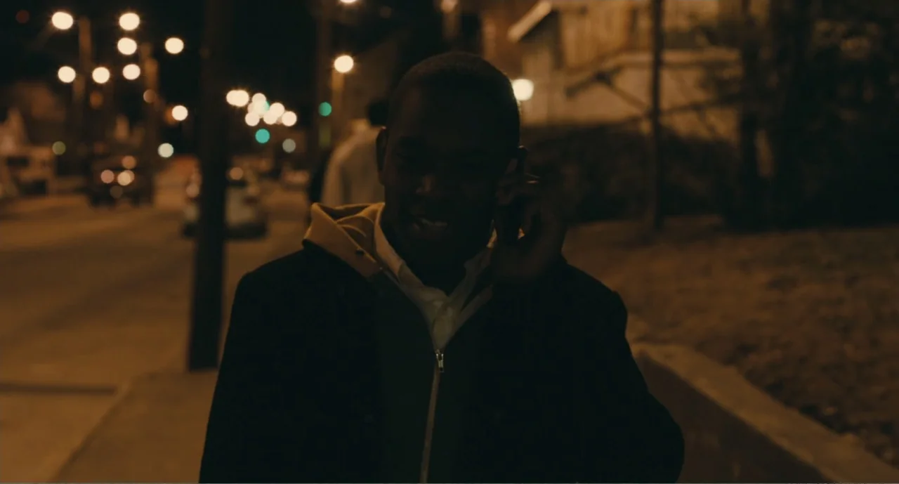 Lila & Eve (2015) movie still: medium — An urban sidewalk at night with blurred streetlights in the background. A man walks forward while talking on…