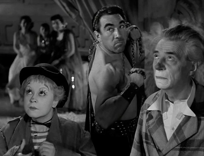La Strada (1954) movie still: medium — A circus tent interior features three performers in costume looking toward a high light source. Two women are…