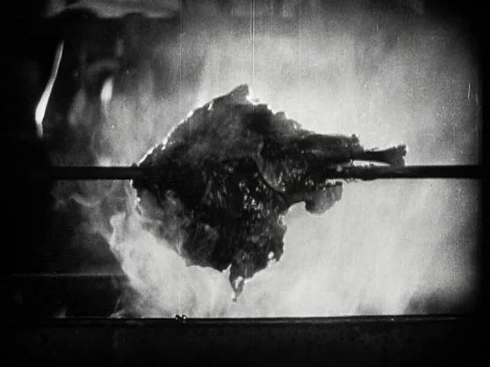The Man Who Laughs (1928) movie still: closeup — A piece of meat rotates on a metal spit over an open fire. Dense white smoke rises around the…