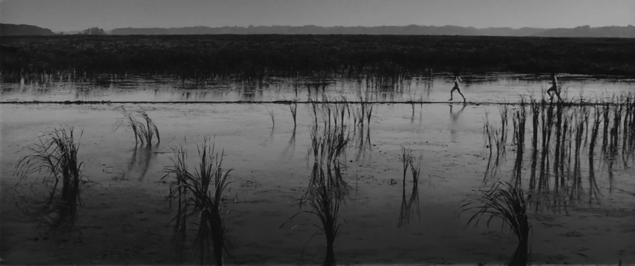 Onibaba (1964) movie still: wide — A vast, flat, muddy marshland stretches toward a low horizon under an overcast sky. Two small human figures run…