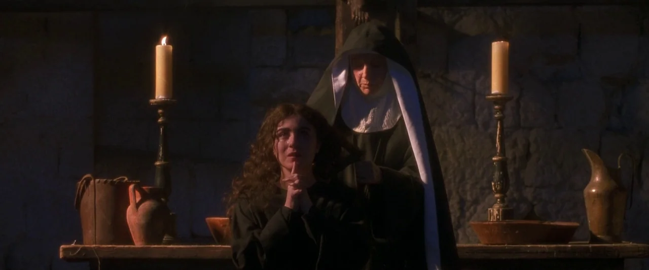 Dangerous Beauty (1998) movie still: medium — A dimly lit room with rough stone walls contains a wooden table with candles. A nun is pinning the…