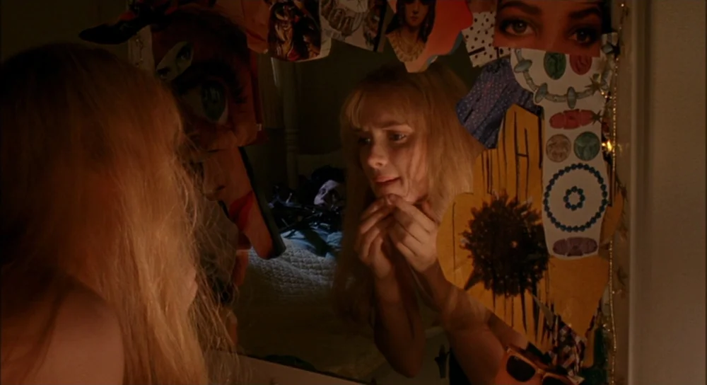 Edward Scissorhands (1990) movie still: medium — A blonde woman peers into a mirror decorated with numerous cut-out magazine collages. She examines…
