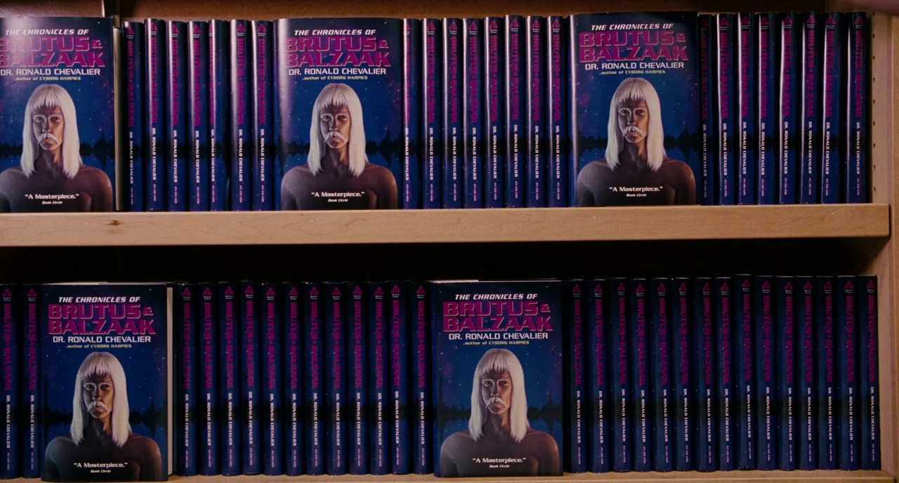 Gentlemen Broncos (2009) movie still: wide — Two wooden shelves are densely packed with multiple copies of the same book. The book covers feature an…