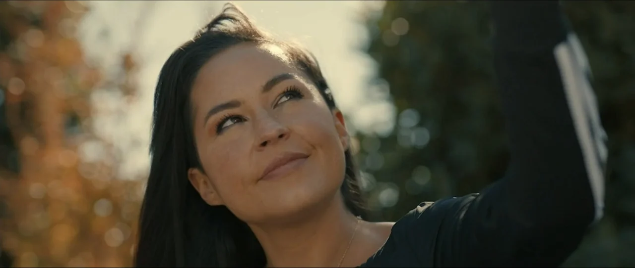 American Sicario (2021) movie still: closeup — An outdoor setting features a woman framed against soft-focus blurred foliage and trees. A woman in a…