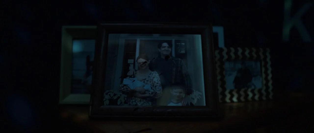 The Boogeyman (2023) movie still: closeup — A dark room contains a collection of framed photographs resting on a wooden surface. A central picture…