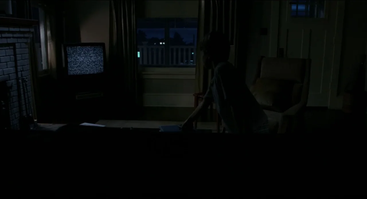 The Ring Two (2005) movie still: medium — A dark living room features a child standing near a television displaying white static. The child reaches…