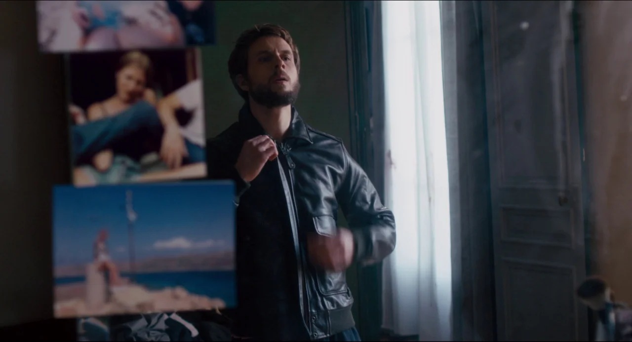 The Night Eats the World (2018) movie still: medium — An interior space contains a man standing near a window draped in white curtains. Several…