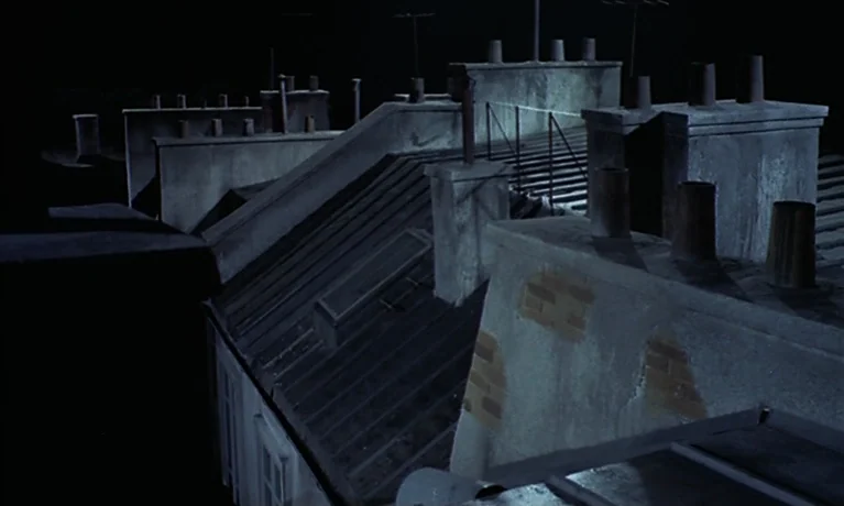Nuits Rouges (1974) movie still: establishing — A collection of residential rooftops features multiple brick chimneys and dark metal shingles. The…