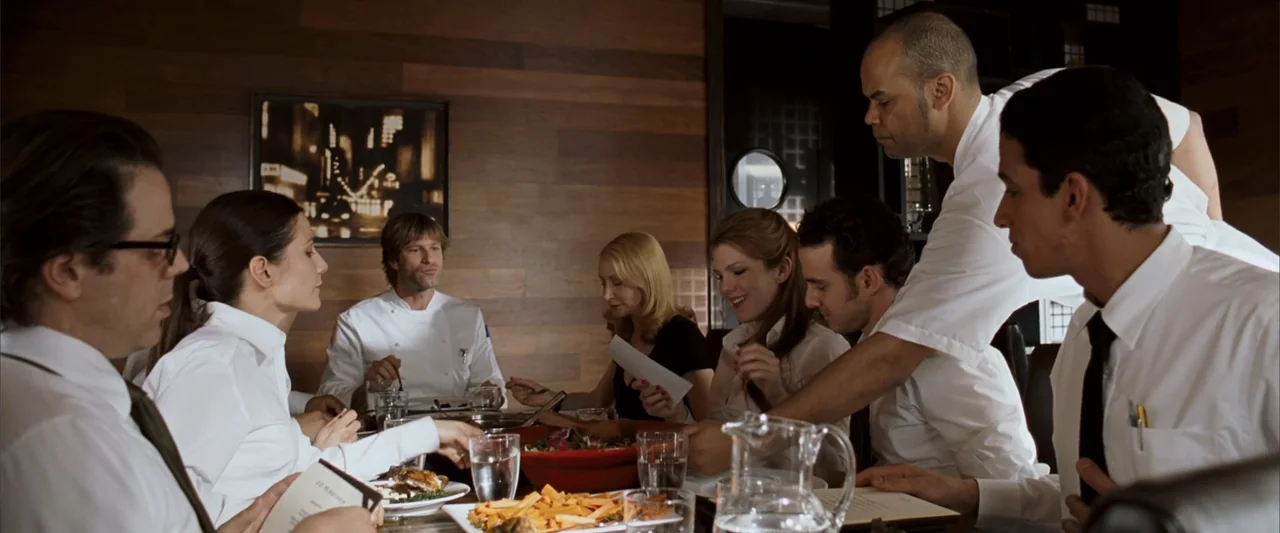 No Reservations (2007) movie still: medium — A modern restaurant interior features wood-paneled walls and a large communal dining table. A group of…