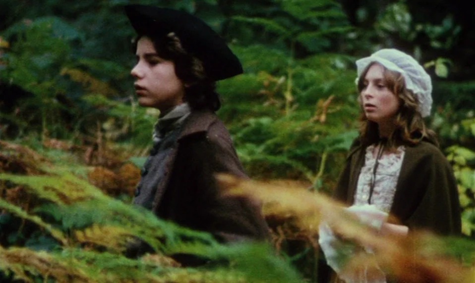 Black Jack (1979) movie still: medium — A dense woodland environment filled with thick green ferns and shadowed foliage. A young man and a young…
