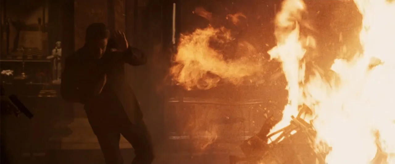 Angels & Demons (2009) movie still: medium — A darkened interior room is lit by a large, intense burst of fire. A man in a dark suit moves away from…