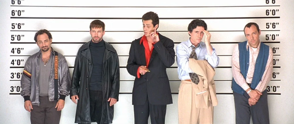 The Usual Suspects movie still: fullbody — A police identification wall features horizontal height markings against a flat white background. Five…