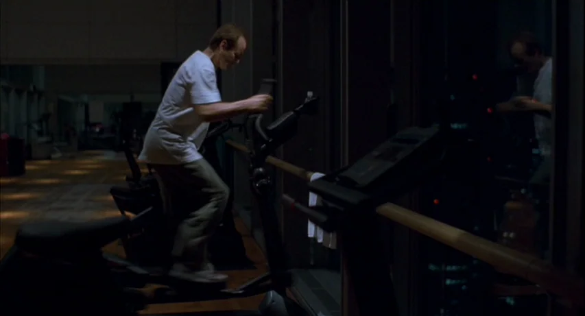 Lost In Translation (2003) movie still: medium — A dimly lit indoor facility with exercise machines positioned near large floor-to-ceiling windows.…