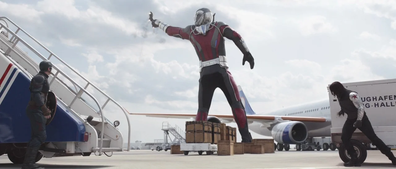 Captain America: Civil War (2016) movie still: wide — A vast airport tarmac displays a parked passenger plane near portable staircases. A giant…
