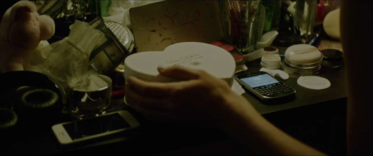 Dogs Don't Wear Pants (2019) movie still: closeup — A cluttered vanity table is covered with cosmetics, electronic devices, and a heart-shaped box.…