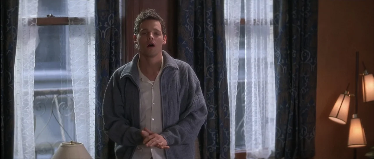 The Wedding Planner (2001) movie still: medium — A room with patterned blue curtains covering large windows and a tiered floor lamp. A young man…