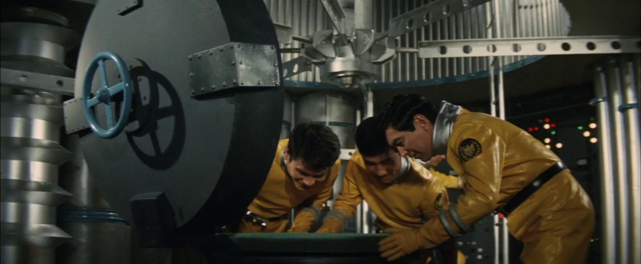 Destroy All Monsters (1968) movie still: medium — A futuristic scientific laboratory features heavy metallic piping and a large open hatch. Three…