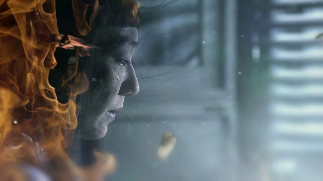 Confessions (2010) movie still: closeup — A dark indoor space is partially illuminated by flames encroaching on the subject. A woman in profile is…