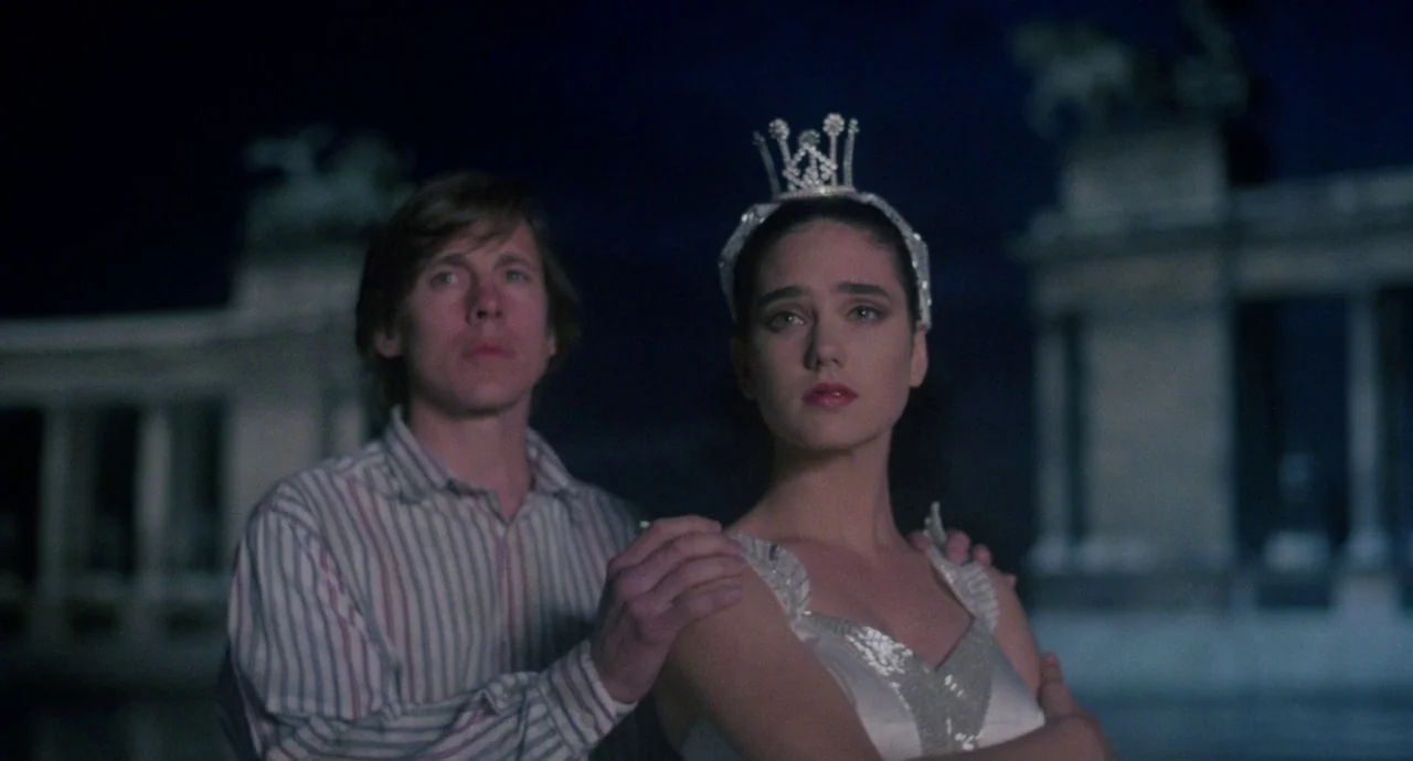 Etoile (1989) movie still: medium — A night scene outside a stone monument with columns and sculptural detailing. A young man stands behind a young…