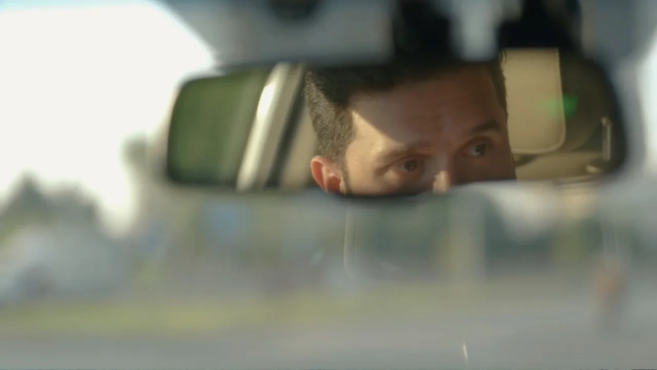 Death Without Mercy (2024) movie still: closeup — A close-up view of a man's face reflected in a car rearview mirror. The man is focused on the road…