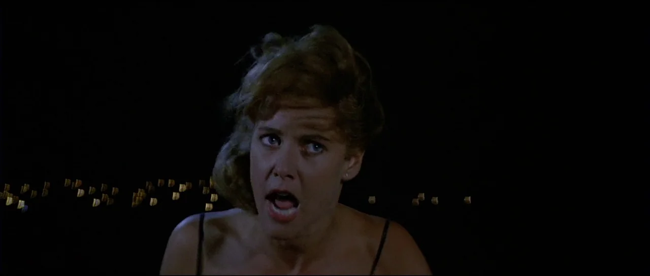 Licence to Kill (1989) movie still: closeup — A woman is captured in a close-up against a pitch-black outdoor nighttime backdrop. She gazes…