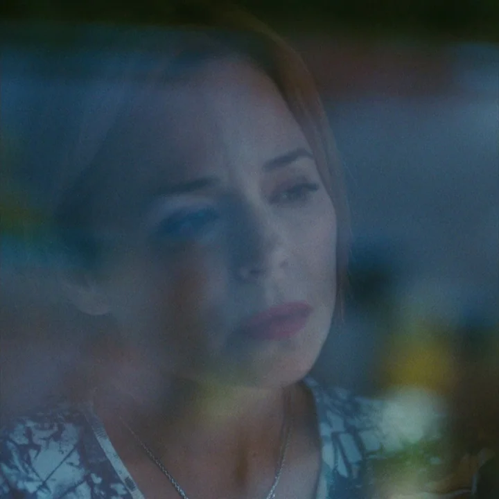 Mommy (2014) movie still: closeup — A woman stares through a reflective pane of glass in a darkened space. The image is layered with light…