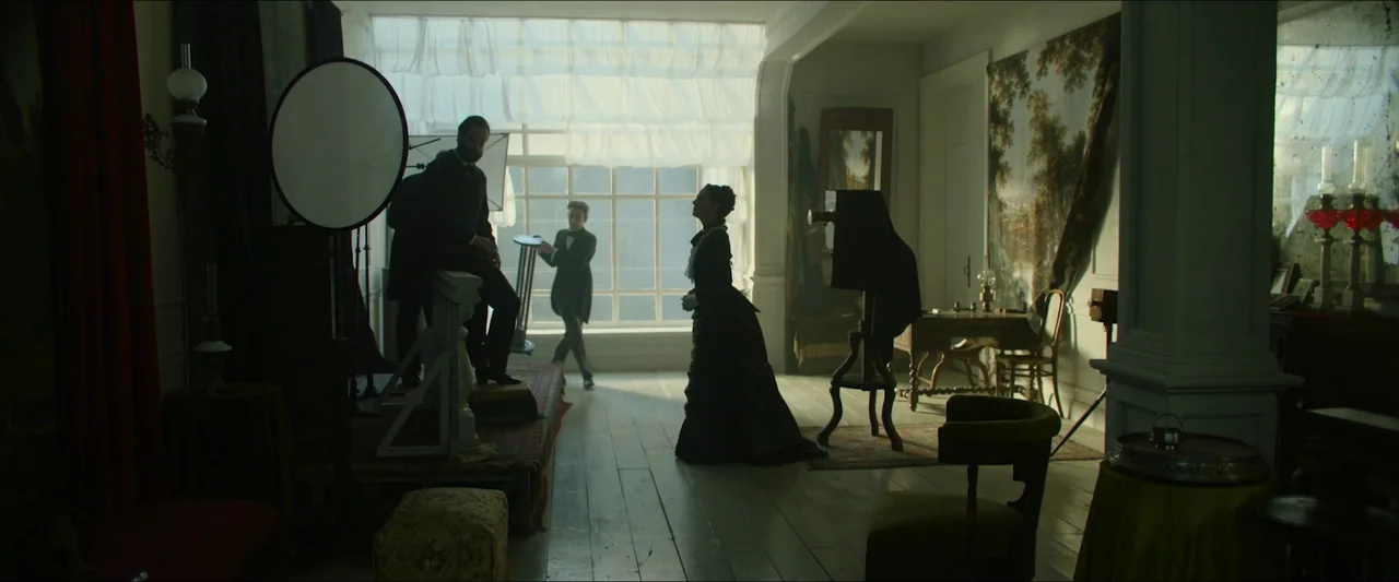 Tchaikovsky’s Wife (2022) movie still: wide — An 1800s photography studio filled with antique equipment and framed by a large window. A woman stands…