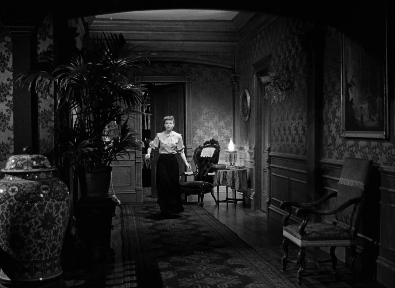 The Spiral Staircase (1946) movie still: fullbody — A dimly lit residential hallway features ornate patterned wallpaper and antique furniture…
