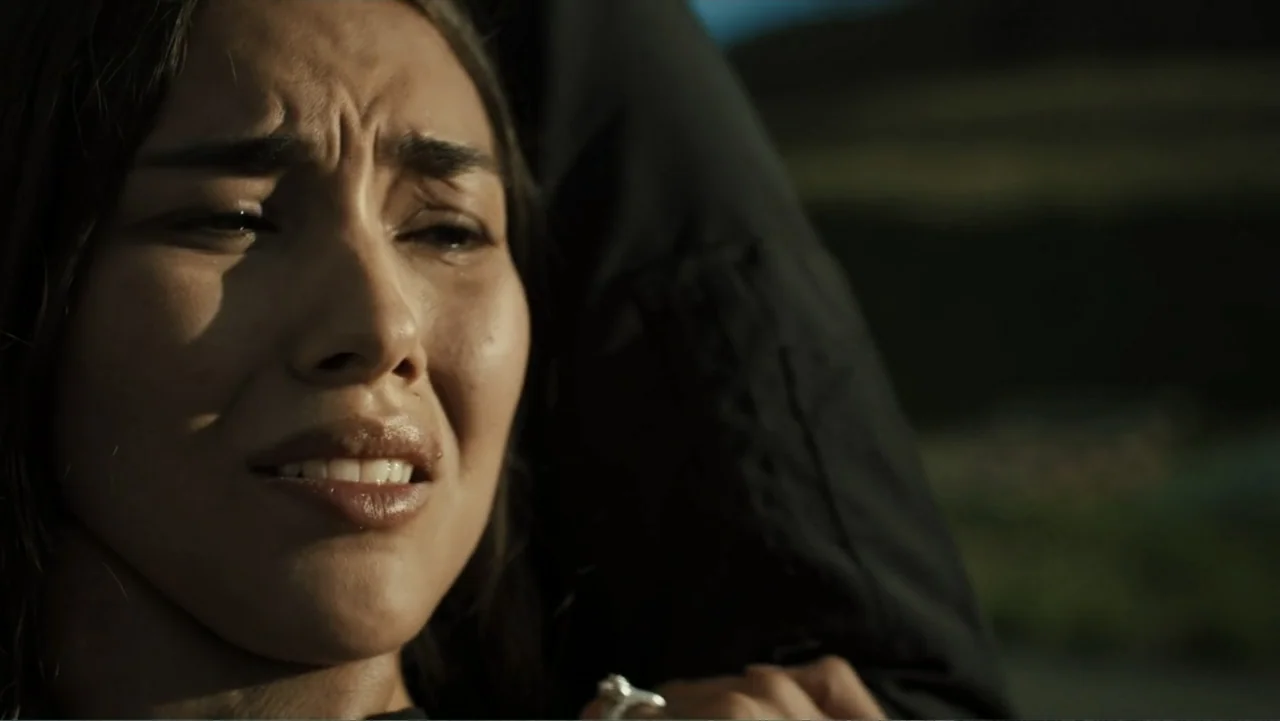 Bullet Proof (2022) movie still: closeup — A dark, blurred hillside landscape provides a dim outdoor background at golden hour. A young woman with…