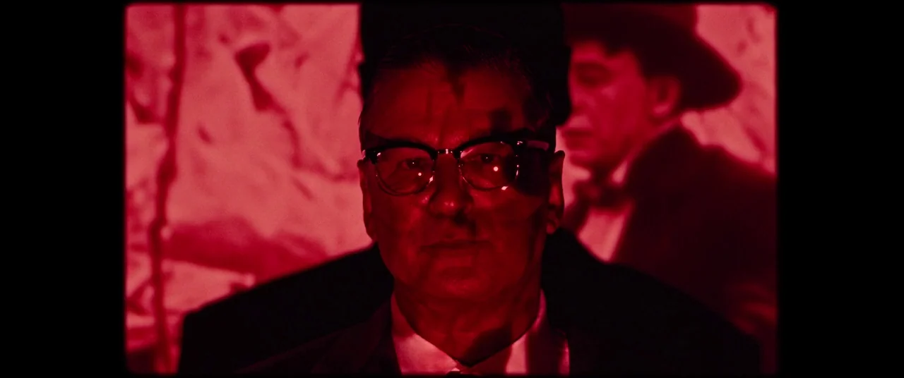 BlacKkKlansman (2018) movie still: closeup — A man stands in an interior space washed entirely in vibrant red light. The man looks forward while a…