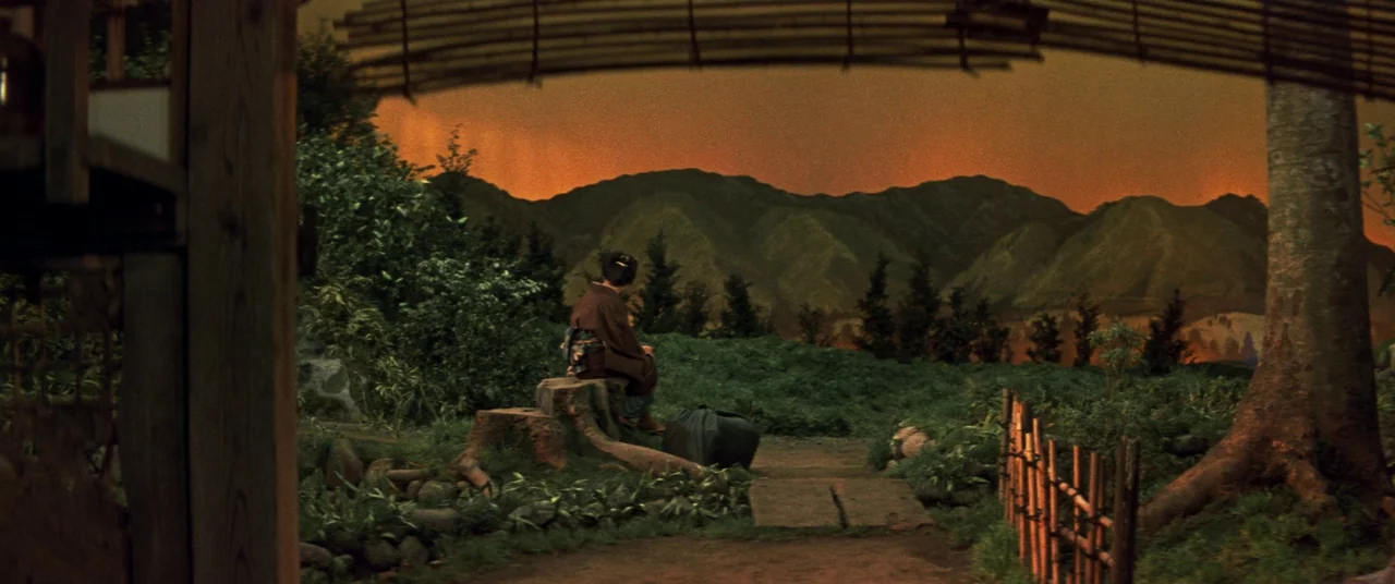 Ballad Of Narayama (1958) movie still: wide — A rural landscape with a dirt path leads towards a distant, vibrant mountain range. A woman sits on a…