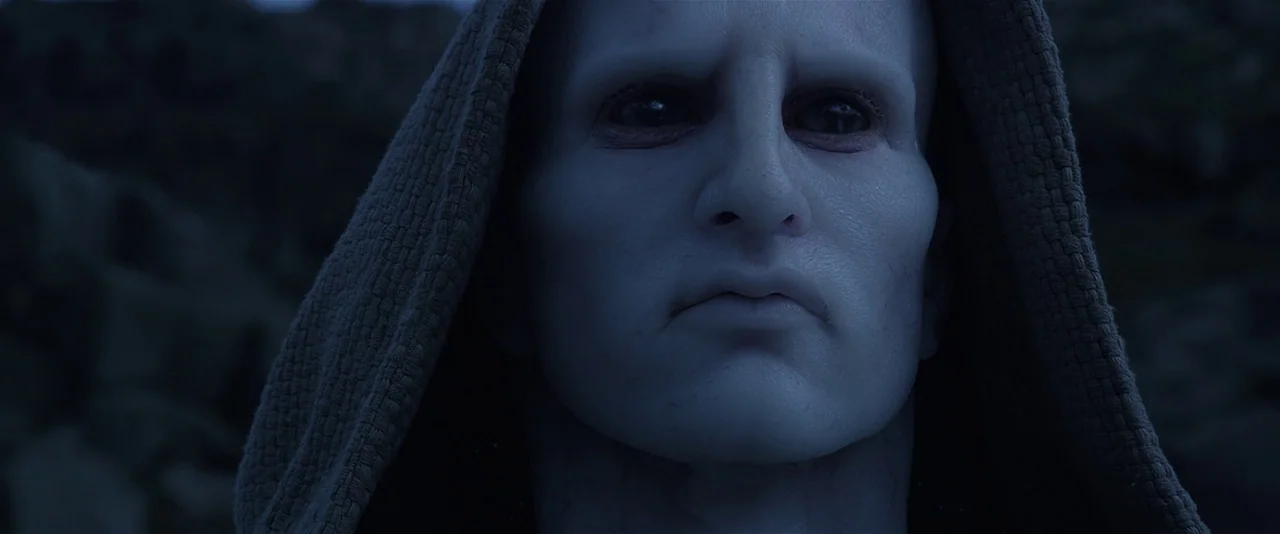 Prometheus (2012) movie still: closeup — A rugged outdoor setting with a dark, textured background of natural rock formations. A pale, hairless…