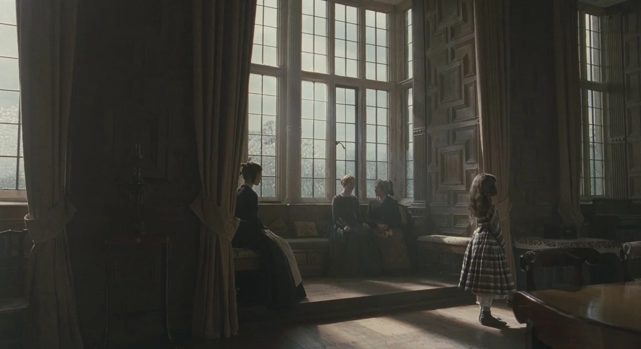 Jane Eyre (2011) movie still: wide — A high-ceilinged room in a historical manor features dark wood paneling and tall windows. Three women converse…