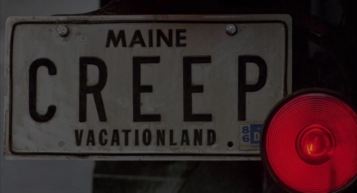 Creepshow 2 (1987) movie still: closeup — A close-up view of a dusty Maine license plate with the word CREEP. A circular red taillight is positioned…