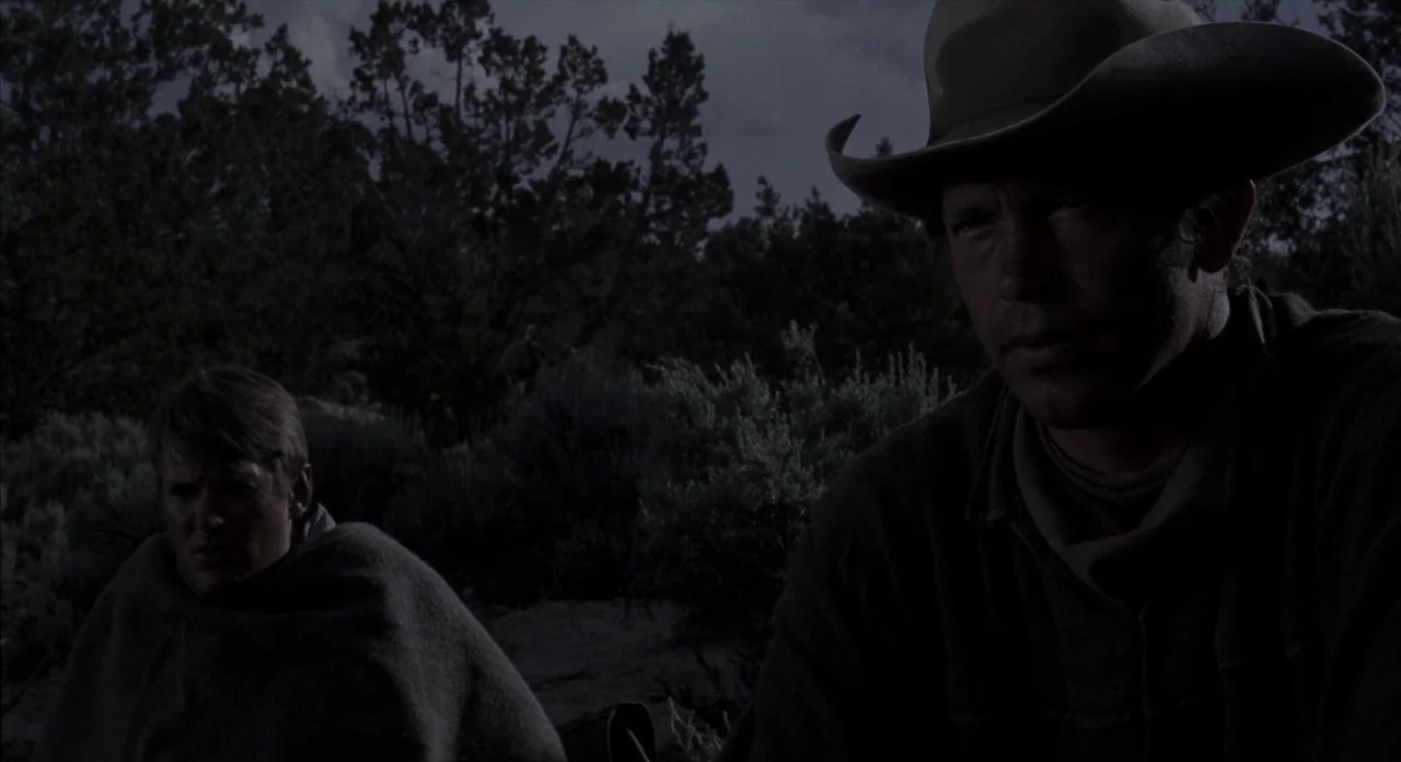 The Shooting (1966) movie still: medium — Two men sit in a dark desert landscape surrounded by low-lying scrub brush at night. The pair sit close…