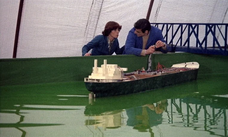 The Man Who Loved Women (1977) movie still: medium — A large indoor testing facility features a long green water tank under a tented roof. Two…
